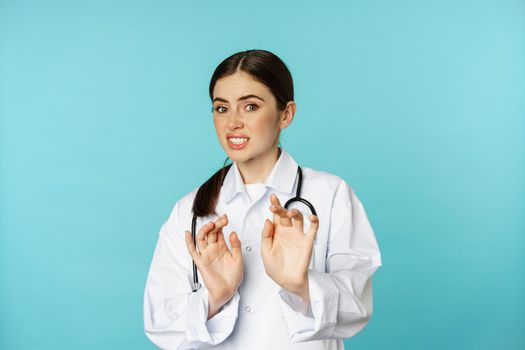 Image of woman doctor cringe, looking with dislike or aversion, rejecting, saying no, stay away, step back from something ugly, standing over torquoise background.
