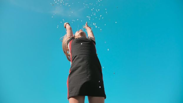 Success concept. Teen girl throws a multi-colored confetti into the blue sky