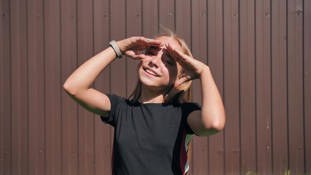 Teen girl closes her eyes from the sun with her hands on a brown background