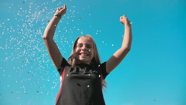 Success concept. Teen girl throws a multi-colored confetti into the blue sky