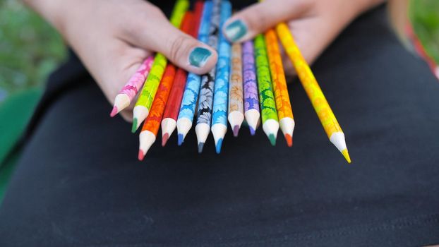 Group of multicolored pencils in young girl's hand. School, colledge and university tools, colorful pencils for drawing graphics and sketching