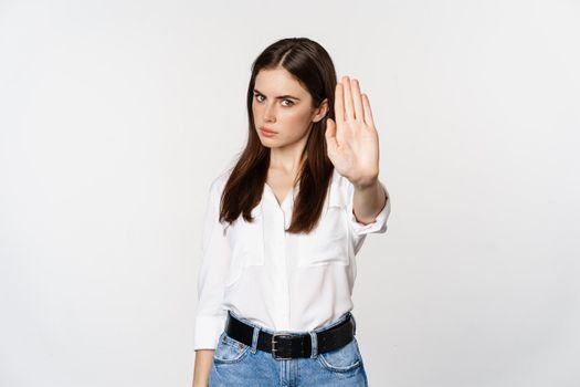 Serious woman showing stop sign, disagree, rejecting smth bad, standing over white background.