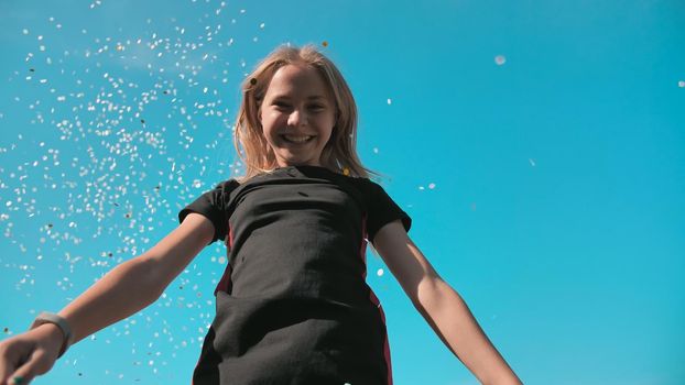 Success concept. Teen girl throws a multi-colored confetti into the blue sky