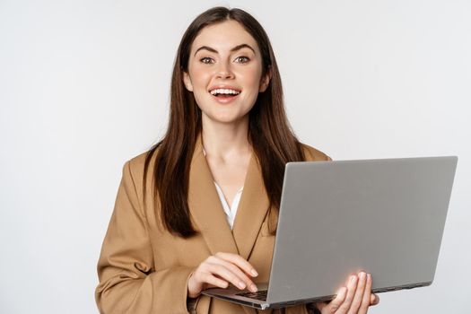 Portrait of corporate woman working with laptop, smiling and looking assertive, white background.