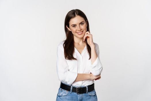 Smiling young businesswoman, female entrepreneur in white shirt, cross arms on chest like professional, standing over studio background.