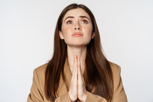 Hopeful corporate woman, student praying, begging god, looking up and pleading, standing over white background. Copy space