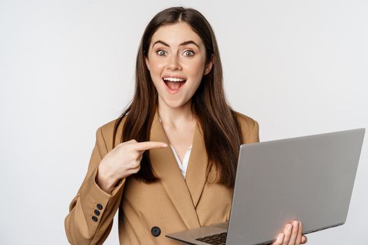Happy businesswoman pointing at laptop screen, showing work progress and smiling excited, standing over white background. Copy space