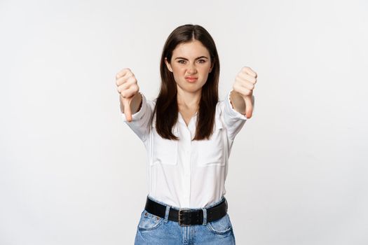 Disappointed adult corporate woman showing thubms down, dislike gesture, negative feedback, complaining and grimacing, white background.