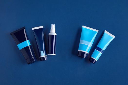 Four colorful different sized tubes and pump bottle with no logo against blue background. Cosmetic packaging, containers. Advertising, branding area. Close up, copy space. Top view, mock up