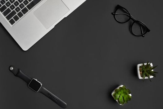 Metallic notebook or laptop, glasses, smartwatch and two green succulents in white pots on black studio background. Modern technology. Close up, copy space. Top view, flat lay, mock up