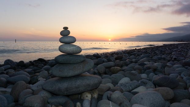 Stack of gray zen stones on the beach at sunset, beautiful seascape. Made of stone tower as rest balance vacation concept.