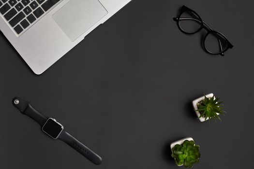 Metallic notebook or laptop, glasses, smartwatch and two green succulents in white pots on black studio background. Modern technology. Close up, copy space. Top view, flat lay, mock up