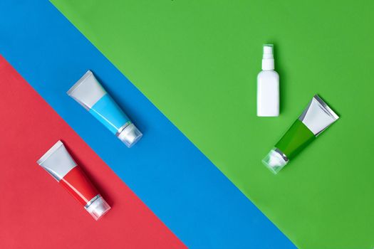 Three cosmetic tubes and white pump bottle with no logo on colorful studio background. Packaging and advertising, branding area. Close up, copy space. Mock up, top view