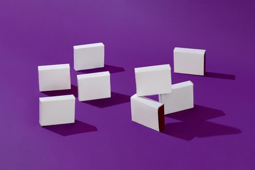 Eight small shadow-casting white cardboard boxes or packs with no label on purple studio background. Branding area. Mock up, advertising. Close up, copy space