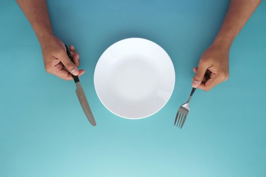 hand holding cutlery with empty plate on wooden table .