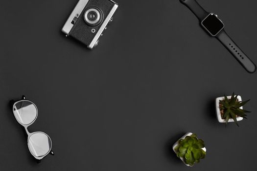 Old vintage camera, glasses, smartwatch and two green succulents in white pots on black studio background. Modern technology. Close up, copy space for your advertising. Top view, flat lay, mock up