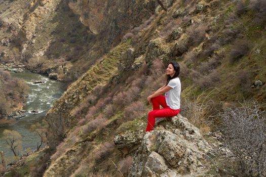 A girl poses on a cliff with a breathtaking view of the gorge in which the river flows. Picturesque photos of mountains.