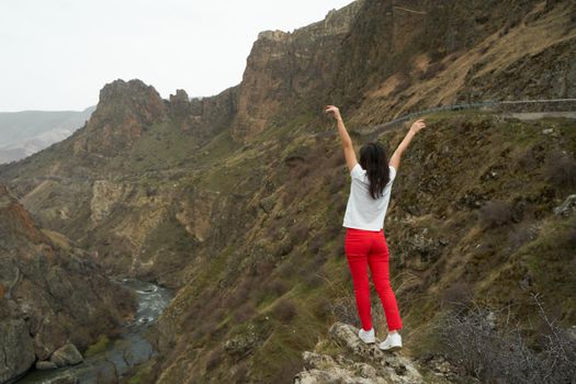 A girl poses on a cliff with a breathtaking view of the gorge in which the river flows. Picturesque photos of mountains.
