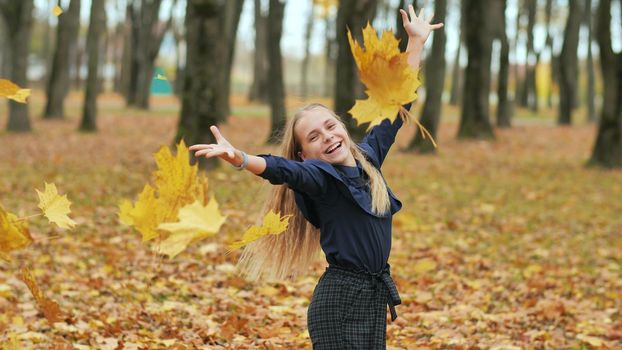 A young girl schoolgirl throws autumn leaves in a city park