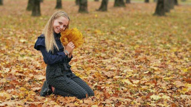 Teenager girl collects autumn leaves in the park and posing