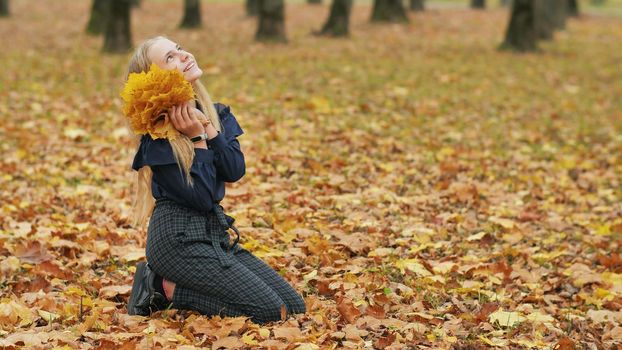 Teenager girl collects autumn leaves in the park and posing