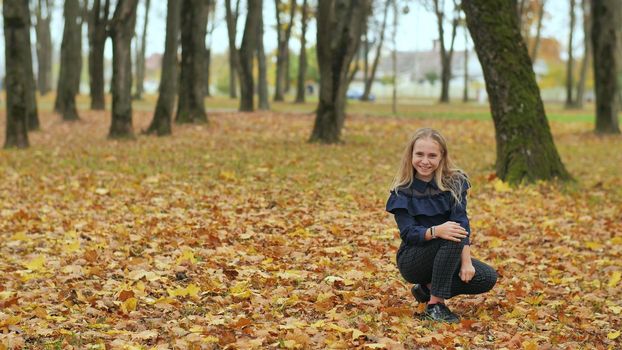 A teenage girl is sitting in an autumn park