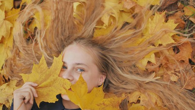 Young happy girl lies in autumn leaves and poses with maples leaves