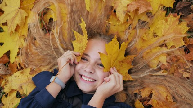 Young happy girl lies in autumn leaves and poses with maples leaves