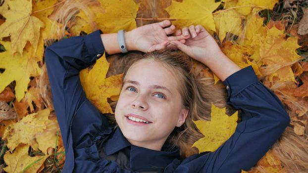 A young happy girl lies in the autumn leaves