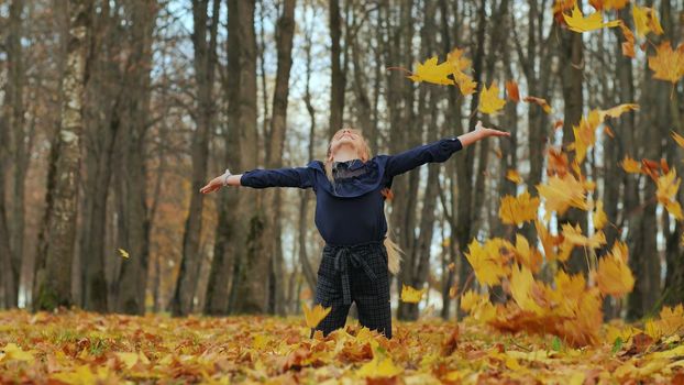 A young girl schoolgirl throws autumn leaves in a city park