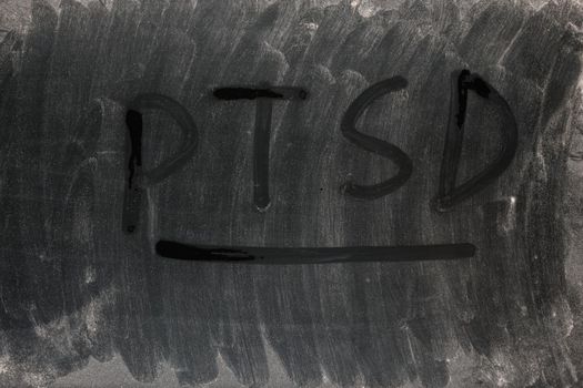 the word PTSD - post traumatic stress disorder handritten on full frame background and texture of dusty black surface of an old LCD screen.
