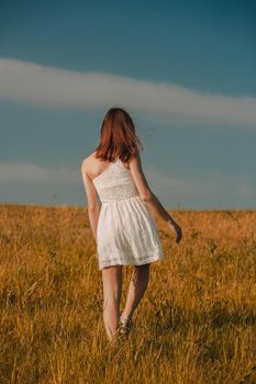 Young beautiful woman walking on a meadow wearing a white dress