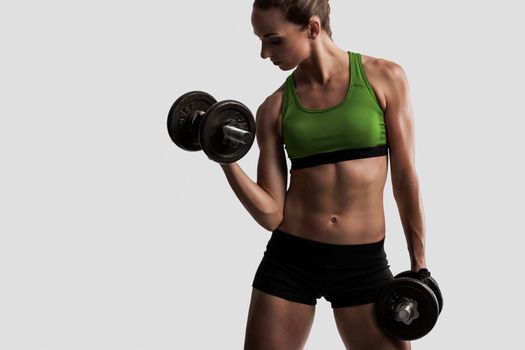 Beautiful young woman in a workout gear lifting dumbbells