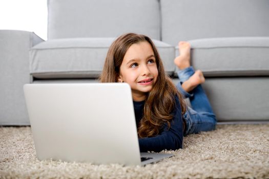 Happy little girl at home working with a laptop