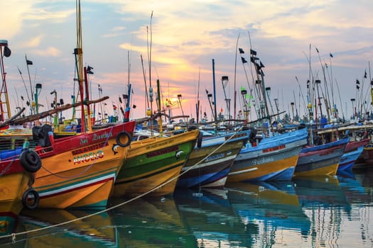 Mirissa, Sri Lanka - April 14, 2017: Colorful boats in Mirissa port with morning sun rising in the background.