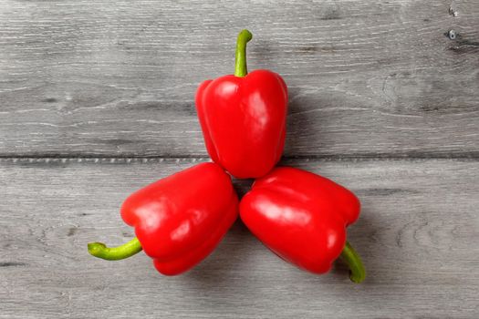 Table top view, three bright red bell peppers arranged into triangle with gray wood desk under.