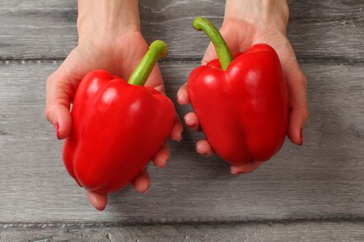 Table top view on young woman hands holding two red bell peppers above gray wood desk.