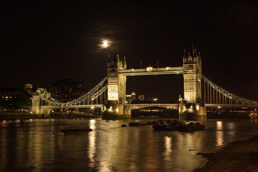 Tower bridge, full moon above, with river Thames illuminated in the night. London, United Kingdom