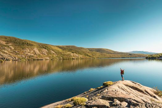 Shot of a man hiking near a beautiful lake with arsm raised