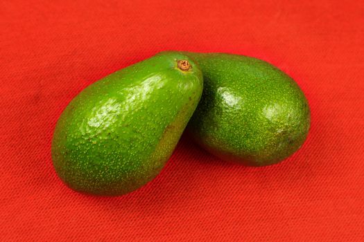 Two whole avocado pears on red tablecloth.