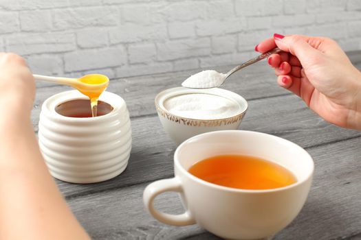 Young woman hands, holding spoon of sugar and honey in other hand deciding what to put in her tea. Artificial vs natural sweetening concept.