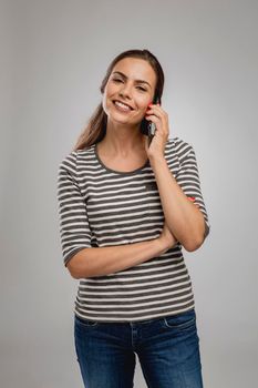 Portrait of beautiful happy young woman over a gray background talking at phone
