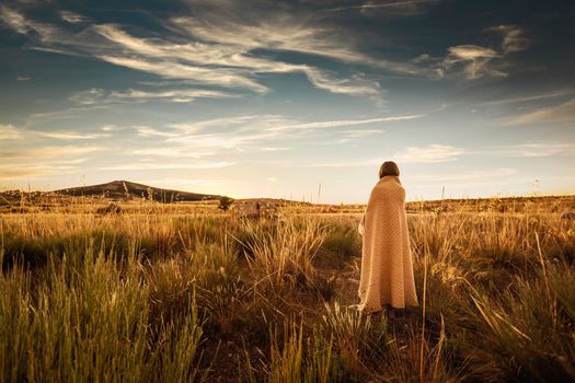 Woman curled up with a yellow blanket at sunset