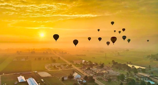 Aerial View of Many Hot Air Balloons Flying into the Sun and Mist On An Early Morning Balloon Festival