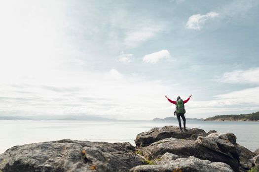 Woman with backpack and arms raised  enjoying the beautiful view of the coast