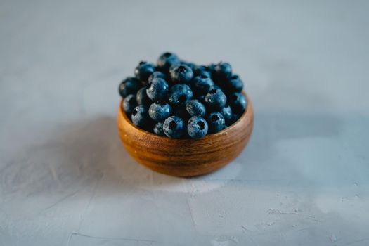 A small wooden bowl with berries on a gray background. Juicy and ripe blueberries in an eco-friendly dish. The concept of healthy eating and nutrition.