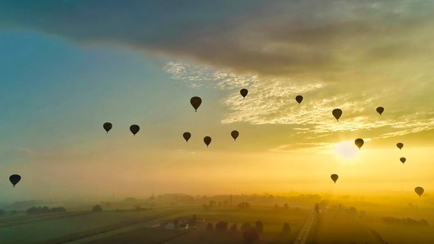 Aerial View of Many Hot Air Balloons Flying into the Sun and Mist On An Early Morning Balloon Festival