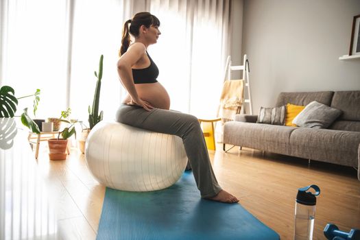 Pregnant woman working out at home doing exercises on a fitball. Keeping in good shape while waiting for baby