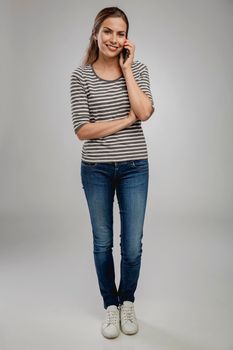 Portrait of beautiful happy young woman over a gray background talking at phone
