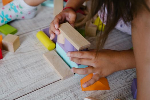 Children's hands build a house from wooden cubes. Colored wooden constructor. Eco-friendly toys for children. A little girl makes a house out of cubes.